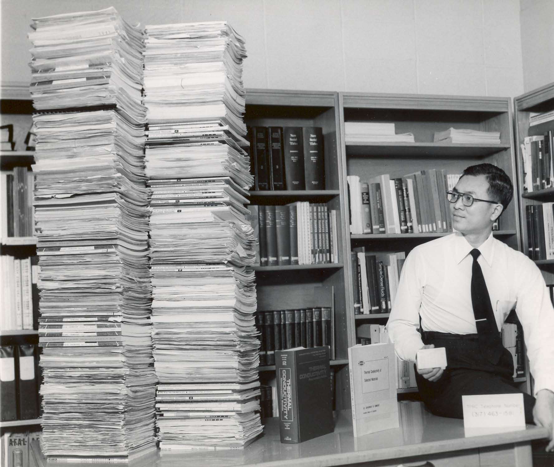 C Y Ho with paper stacks of handbooks